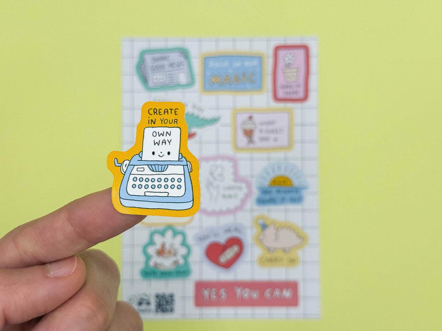 Sheet of decorative stickers with motivational phrases and a typewriter illustration on a yellow background.