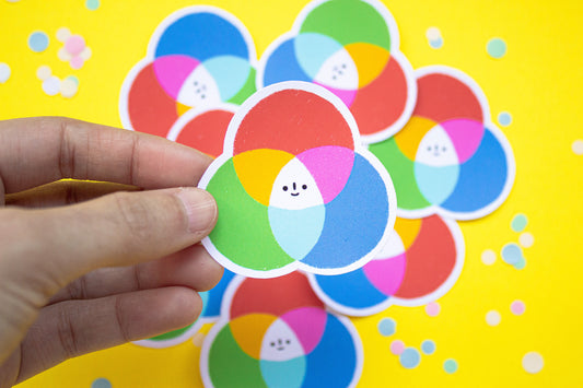 Circular stickers of a color wheel with smiley faces held by a hand against a yellow background