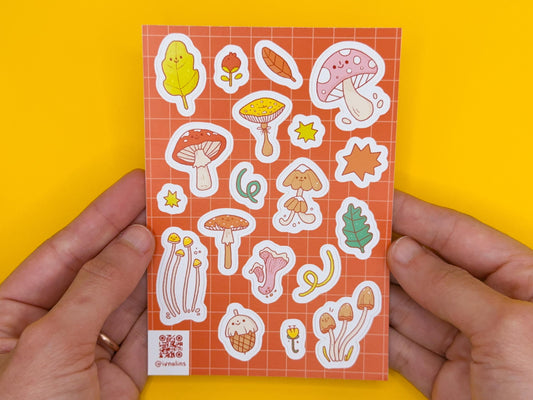 Sticker sheet with various illustrations held by hands against a yellow background