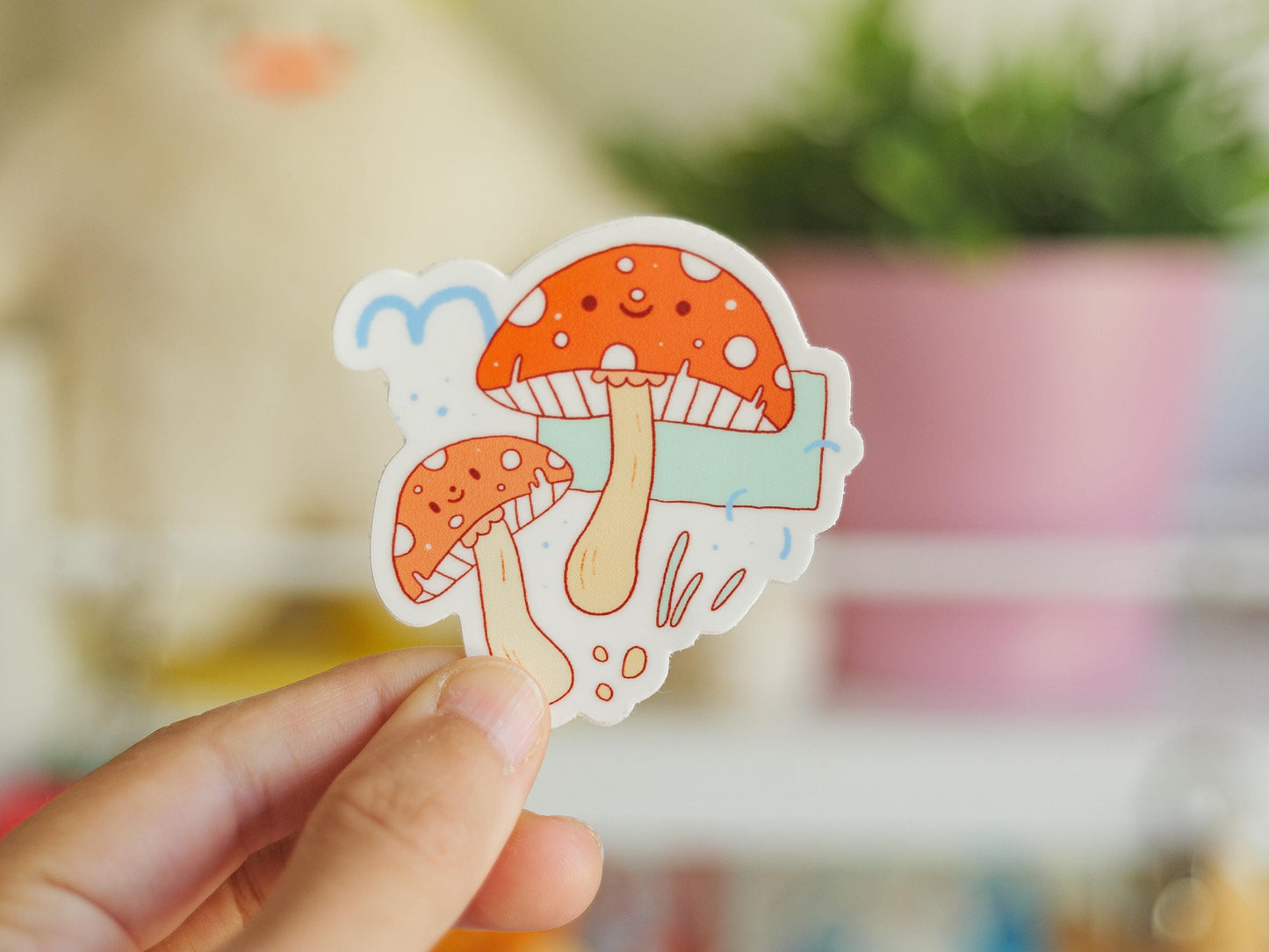 Hand holding a colorful mushroom sticker with a blurred indoor background