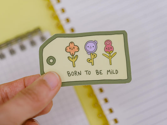 Sticker with flowers and 'Born to be Mild' text held by a hand on a notebook background