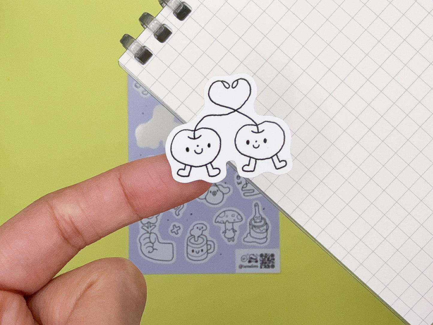 Hand holding a clear stamp with cartoon apple and cherry design on a green background