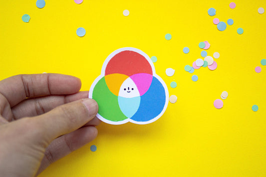 Hand holding a colorful color wheel diagram sticker with confetti on a yellow background