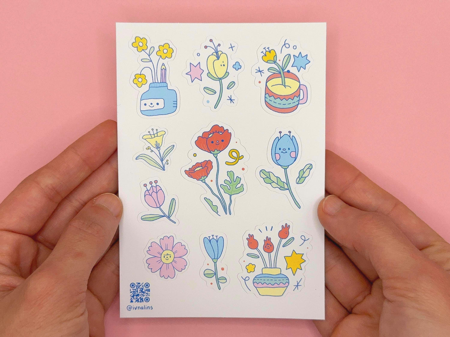 Sheet of colorful floral stickers held by hands against a pink background