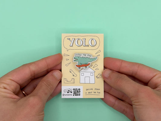 Small yellow card with 'YOLO' design held between two hands against a light green background. The pin says "enjoy the ride"