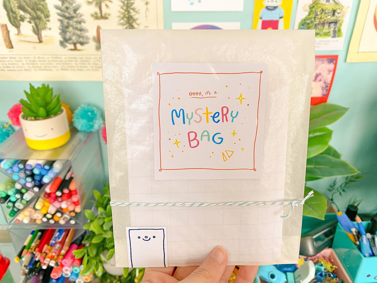 Mystery bag with colorful text held in front of a colorful background with stationery items.