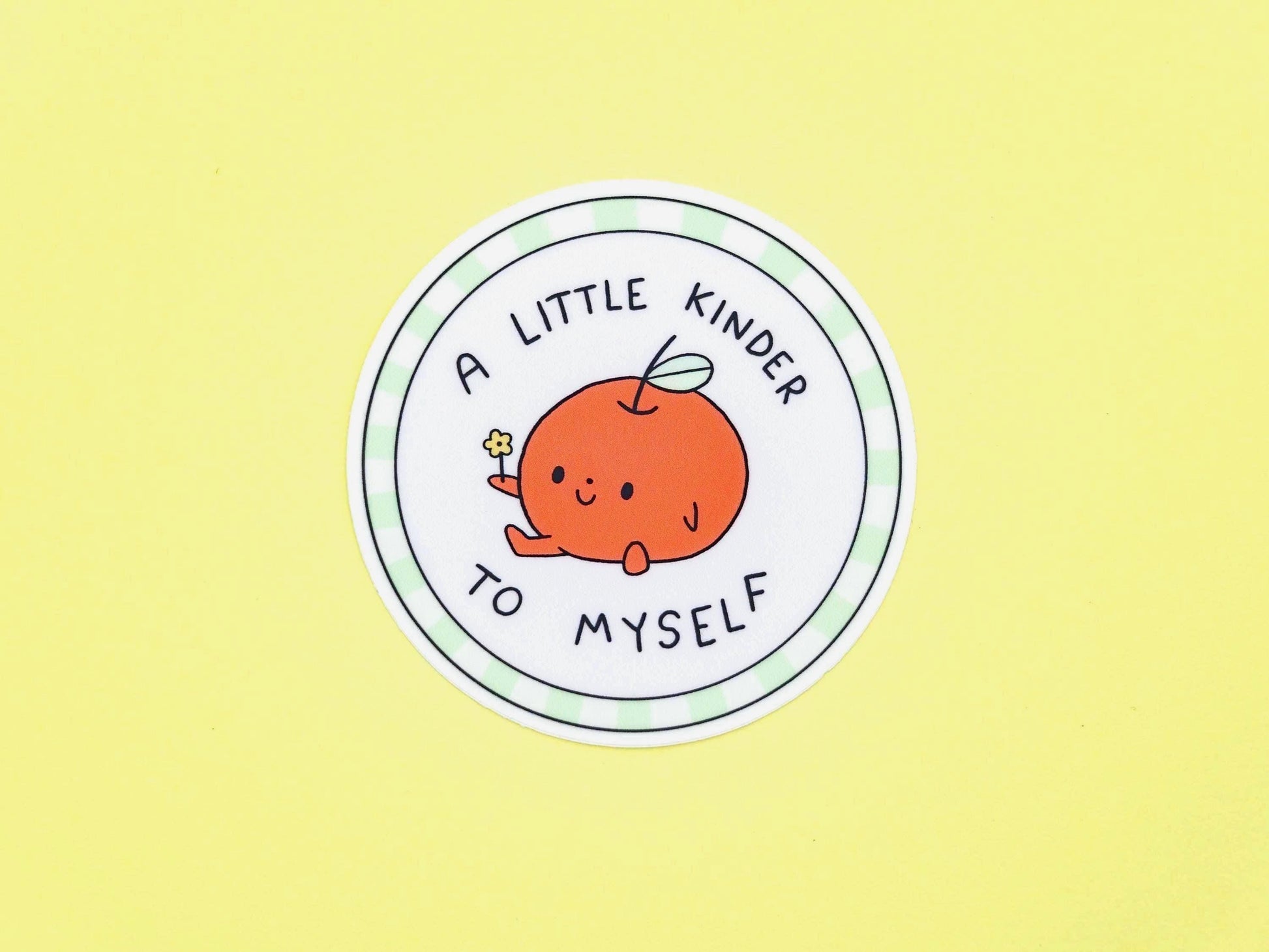 Circular sticker with a cartoon apple and text 'A little kinder to myself' on a yellow background