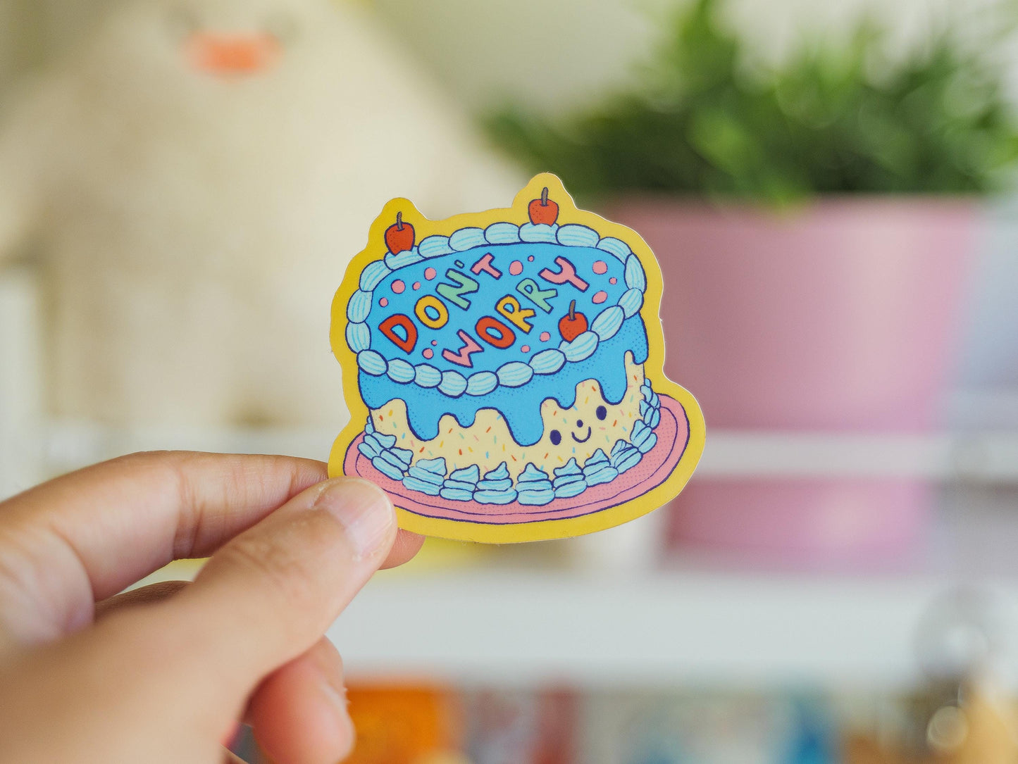 Colorful sticker with 'Don't Worry' text held by a hand against a blurred indoor background