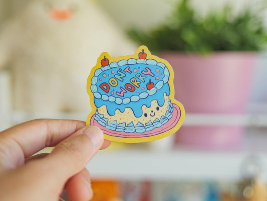Colorful sticker with 'Don't Worry' text held by a hand against a blurred indoor background