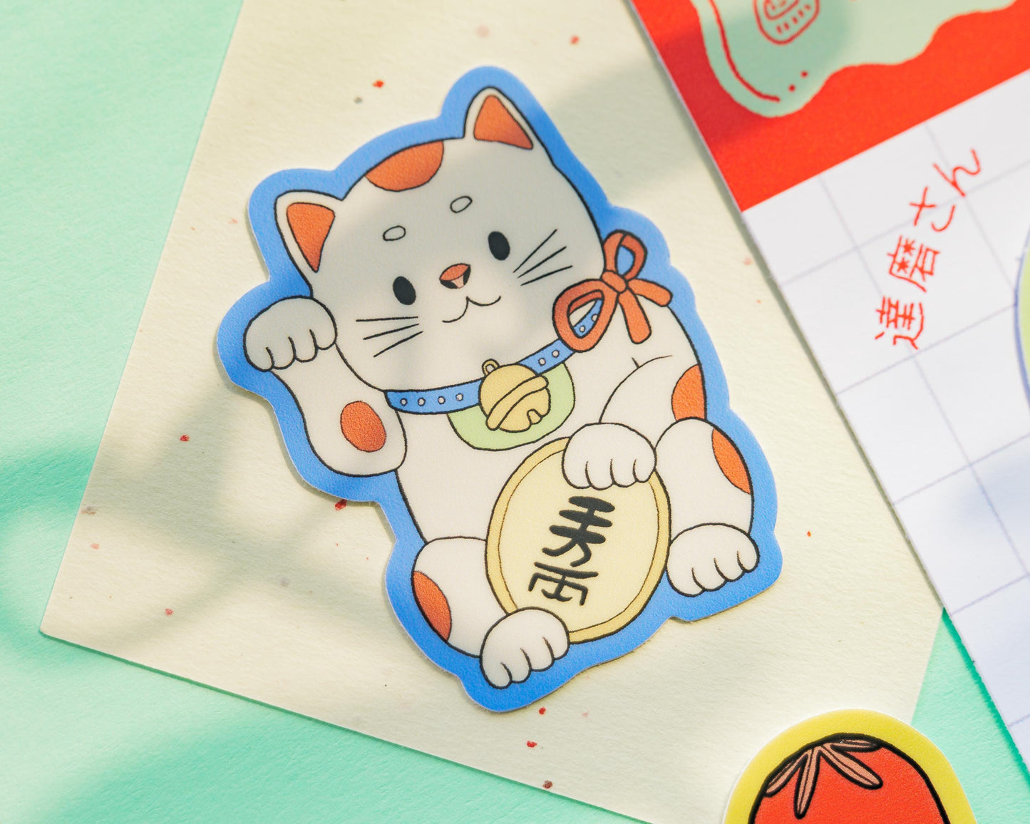 Sticker of a cartoon cat maneki neko with a blue border on a light green background
