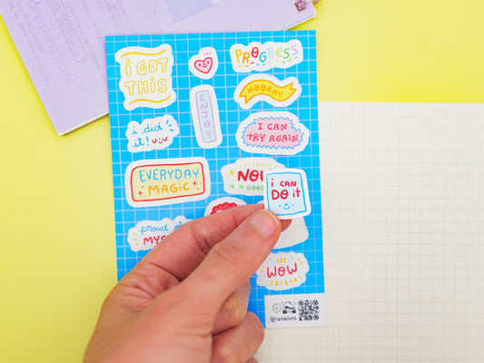 Hand holding a sticker with motivational phrases on a colorful background