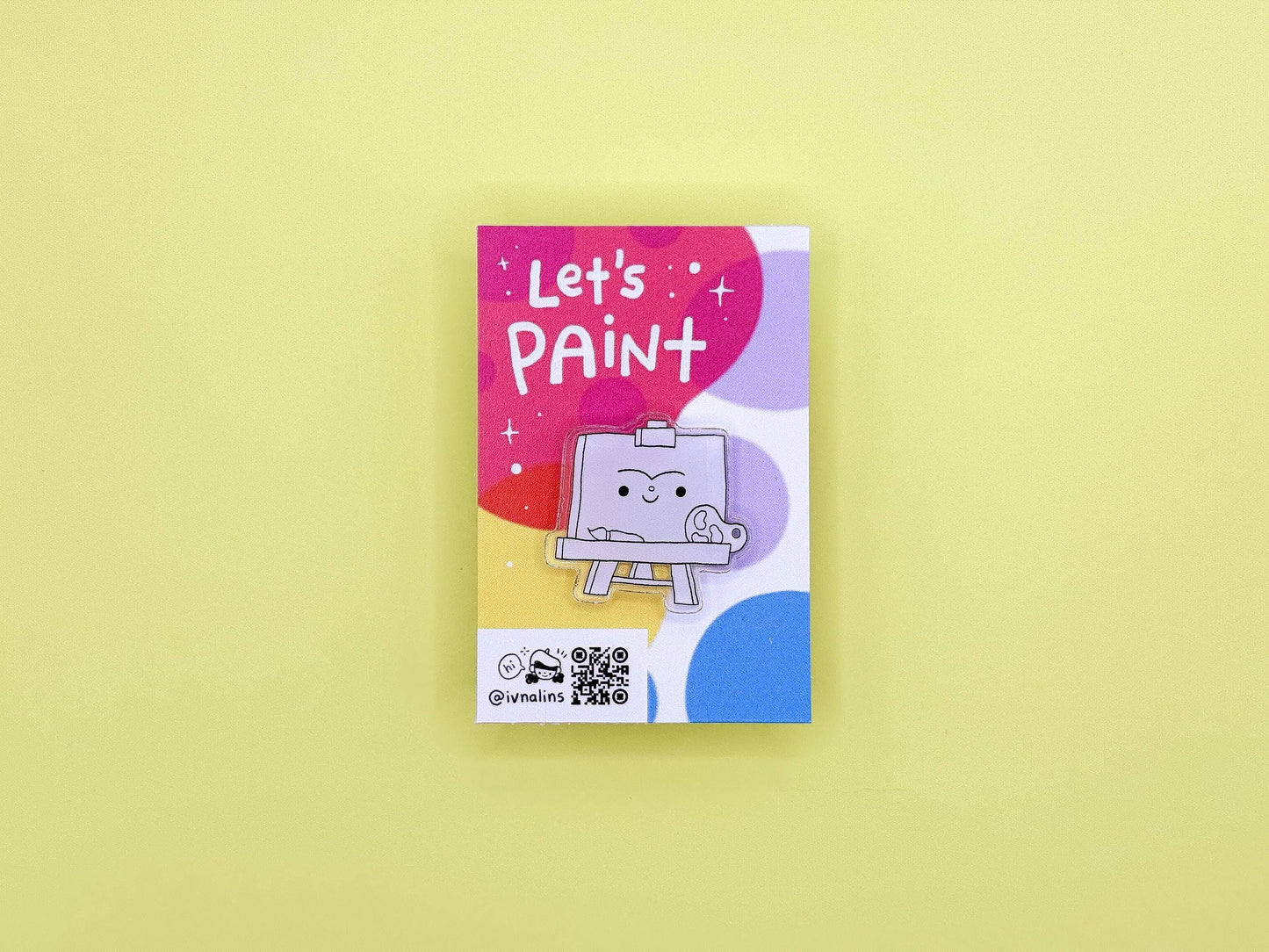 Colorful packaging of a pin with a smiling painting easel design with 'Let's Paint' text on a yellow background