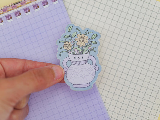 Hand holding a sticker of a vase with flowers on checkered paper