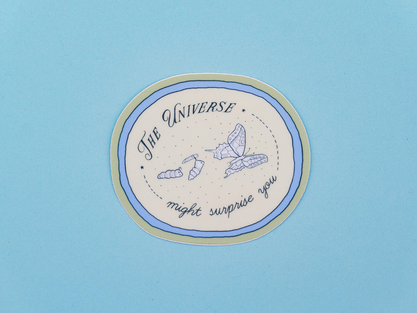 Circular sticker with text saying "the universe might surprise you" and illustrations of a catterpillar turning into a chrysalis and butterfly, on a blue background