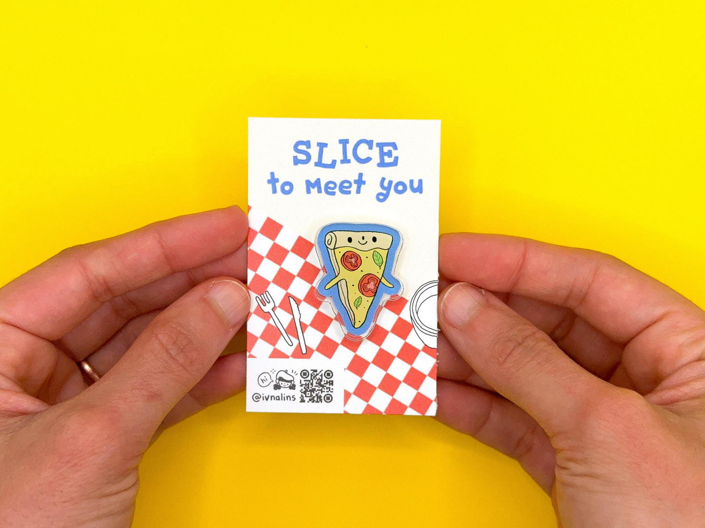 Hand holding a small card with a pizza slice pin design and text on a yellow background