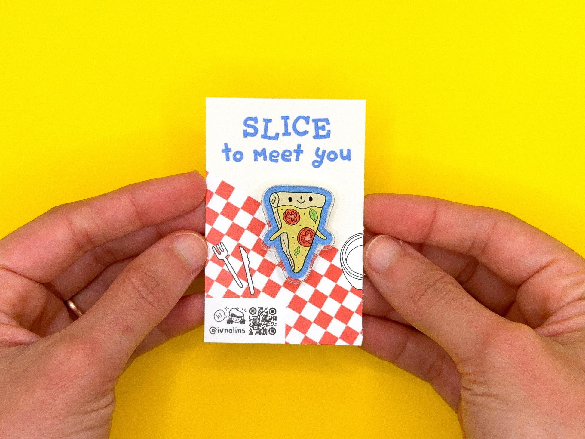 Hand holding a small card with a pizza slice pin design and text on a yellow background