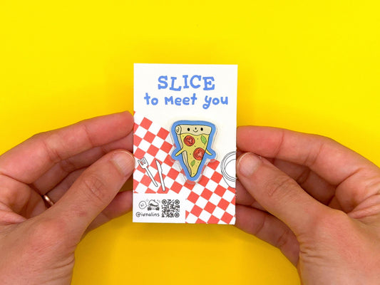 Hand holding a small card with a pizza slice pin design and text on a yellow background