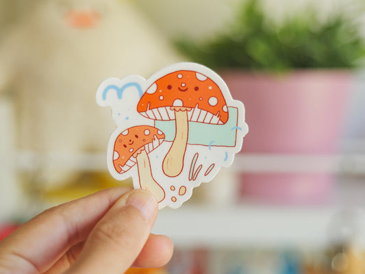 Hand holding a colorful mushroom sticker with a blurred indoor background