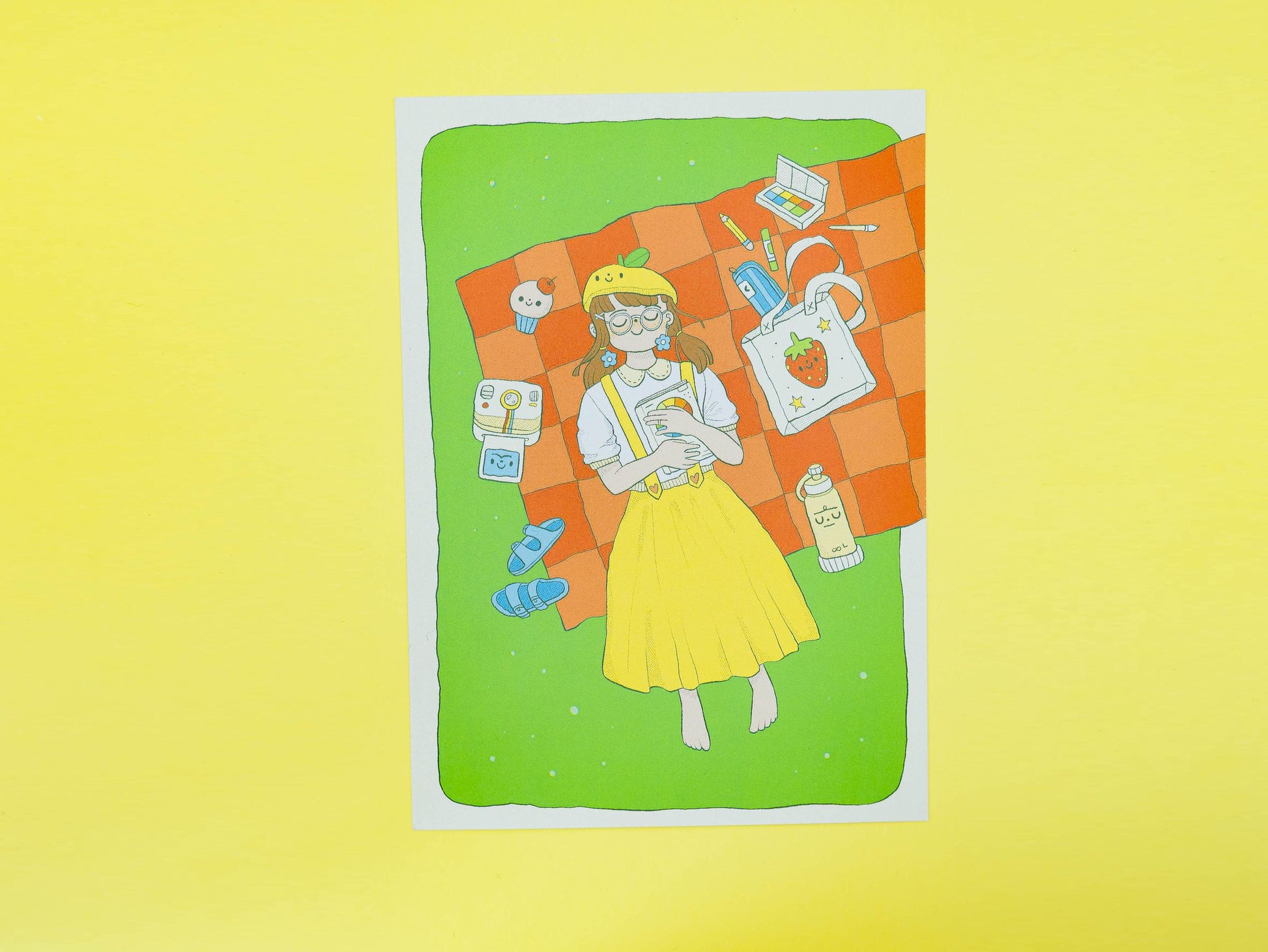 Illustration of a person on a picnic with art supplies and a bag filled with baked goods and objects on a green background with a yellow border