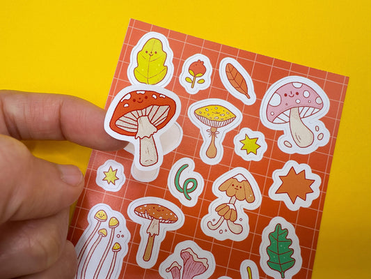 Sheet of colorful mushroom and leaf stickers held by a hand on a yellow background