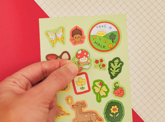 Hand holding a sheet of colorful stickers with nature-themed designs on a red and white checkered background.