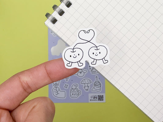 Hand holding a clear stamp with cartoon apple and cherry design on a green background
