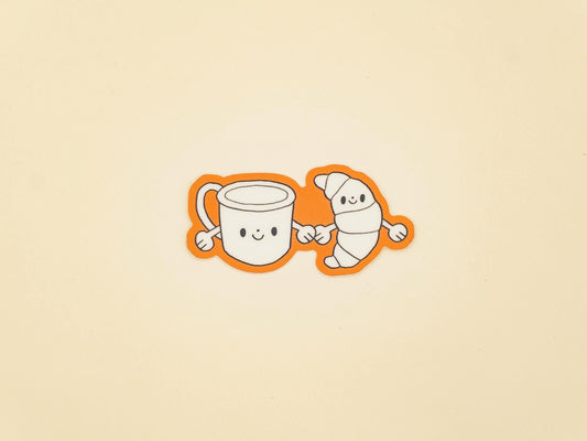 Two cartoon characters, a mug and a croissant, holding hands on a beige background.