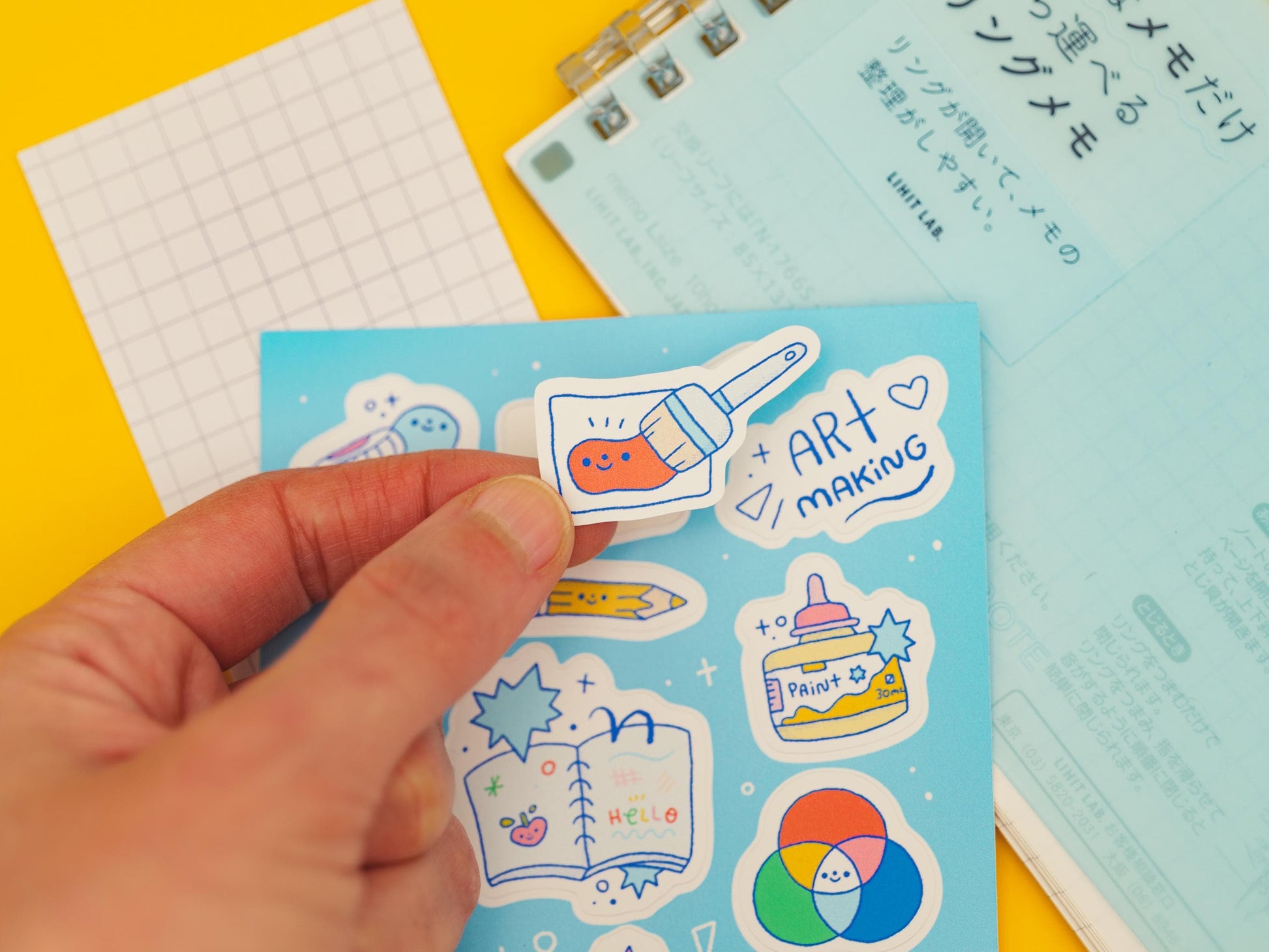 Hand holding a blue card with colorful stickers on a yellow background
