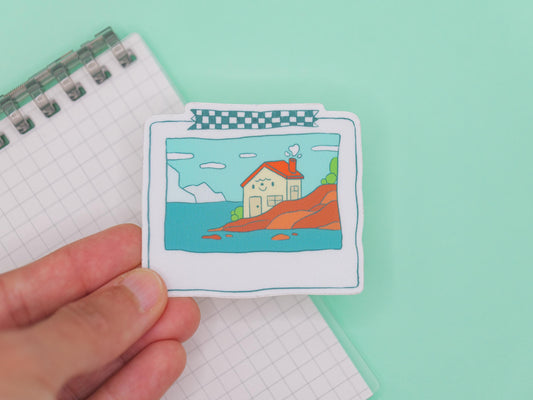 Small illustration of a house on a hill held by a hand against a light green background