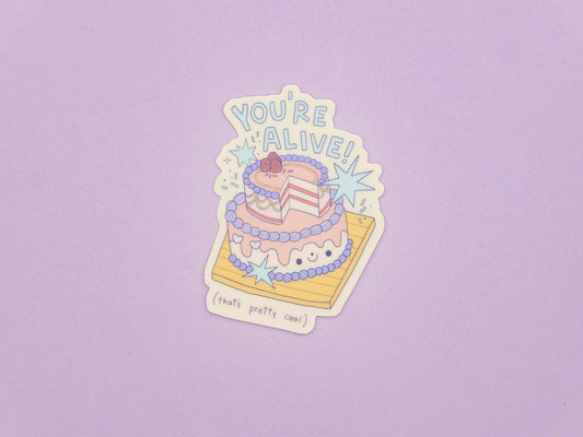 Sticker of a cake with 'You're Alive!' text on a purple background