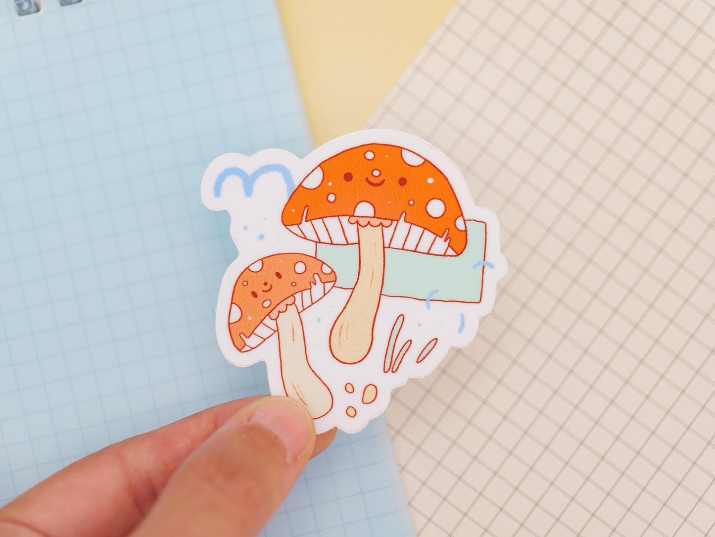 Sticker of mushrooms held by a hand on a light blue and grid-patterned background