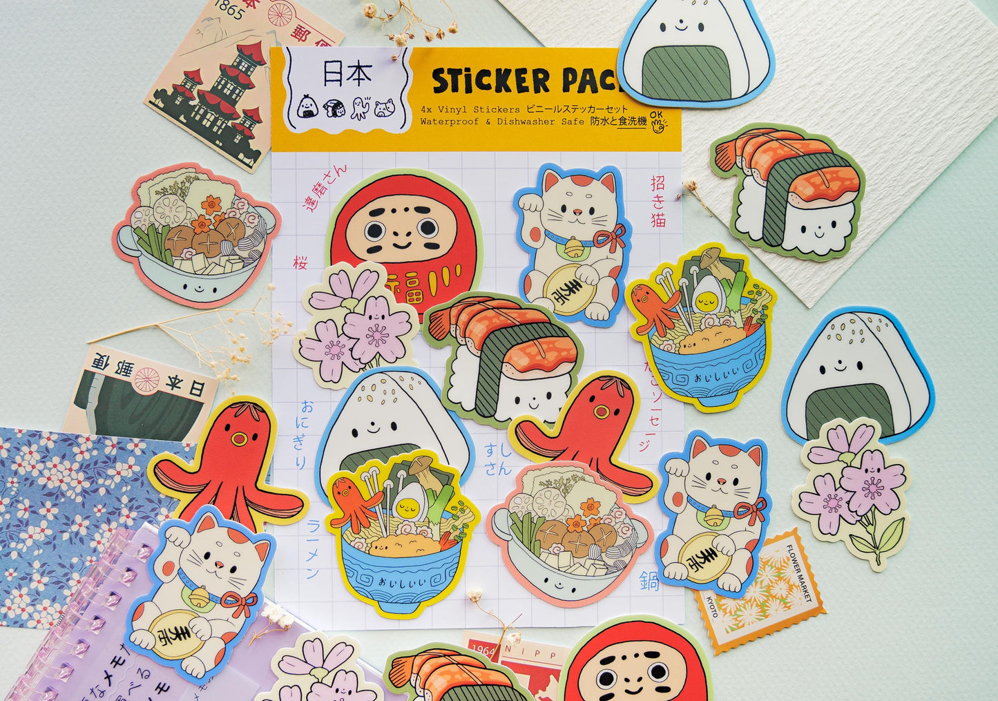 Sticker pack with various cute illustrations on a light blue background. Maneki Neko, Daruma, Sakura Flower, Sushi, Onigiri, Tako Sausage, Ramen and Nabe
