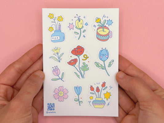 Sheet of colorful floral stickers held by hands against a pink background