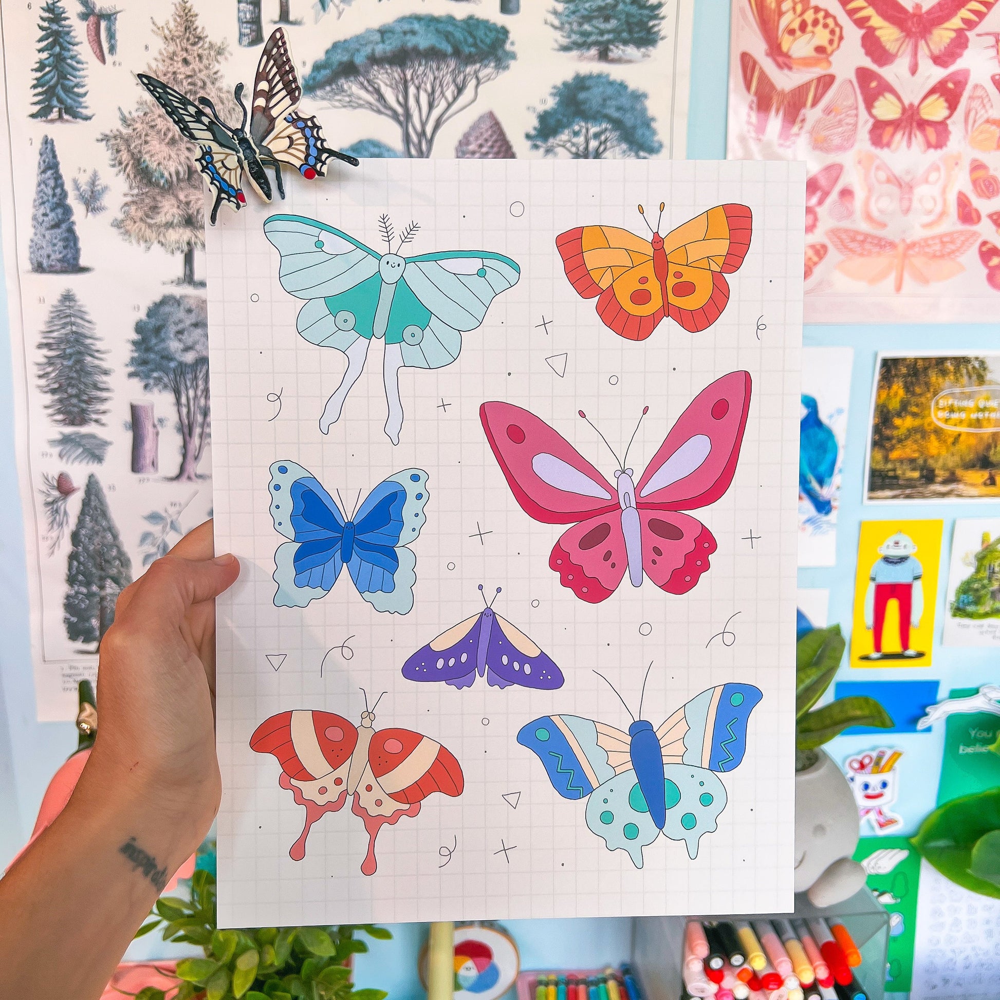 Sheet of colorful butterfly illustrations held by a hand with a multicolored background.