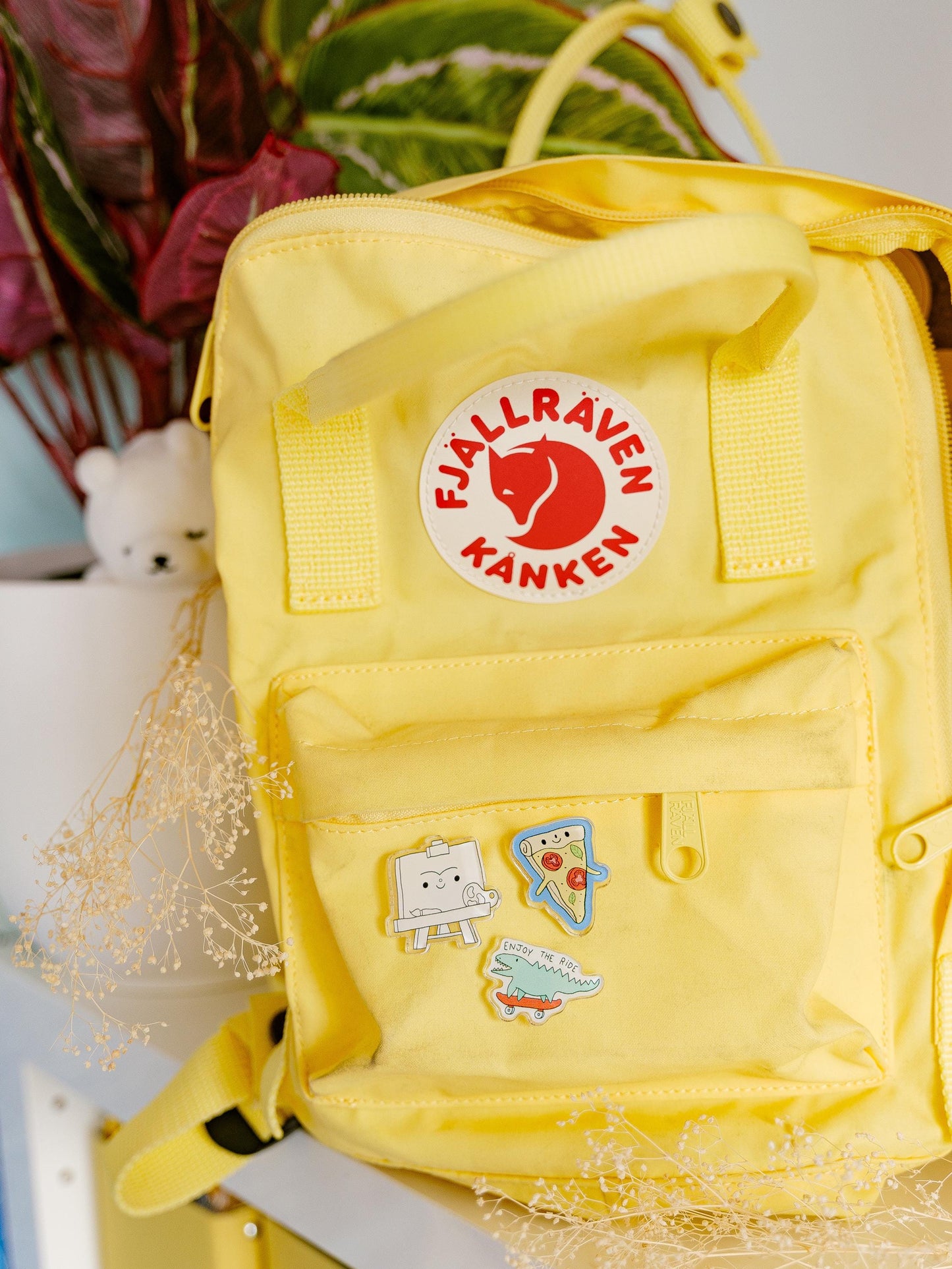 Yellow backpack with Fjällräven Kånken logo and pins on a blurred background