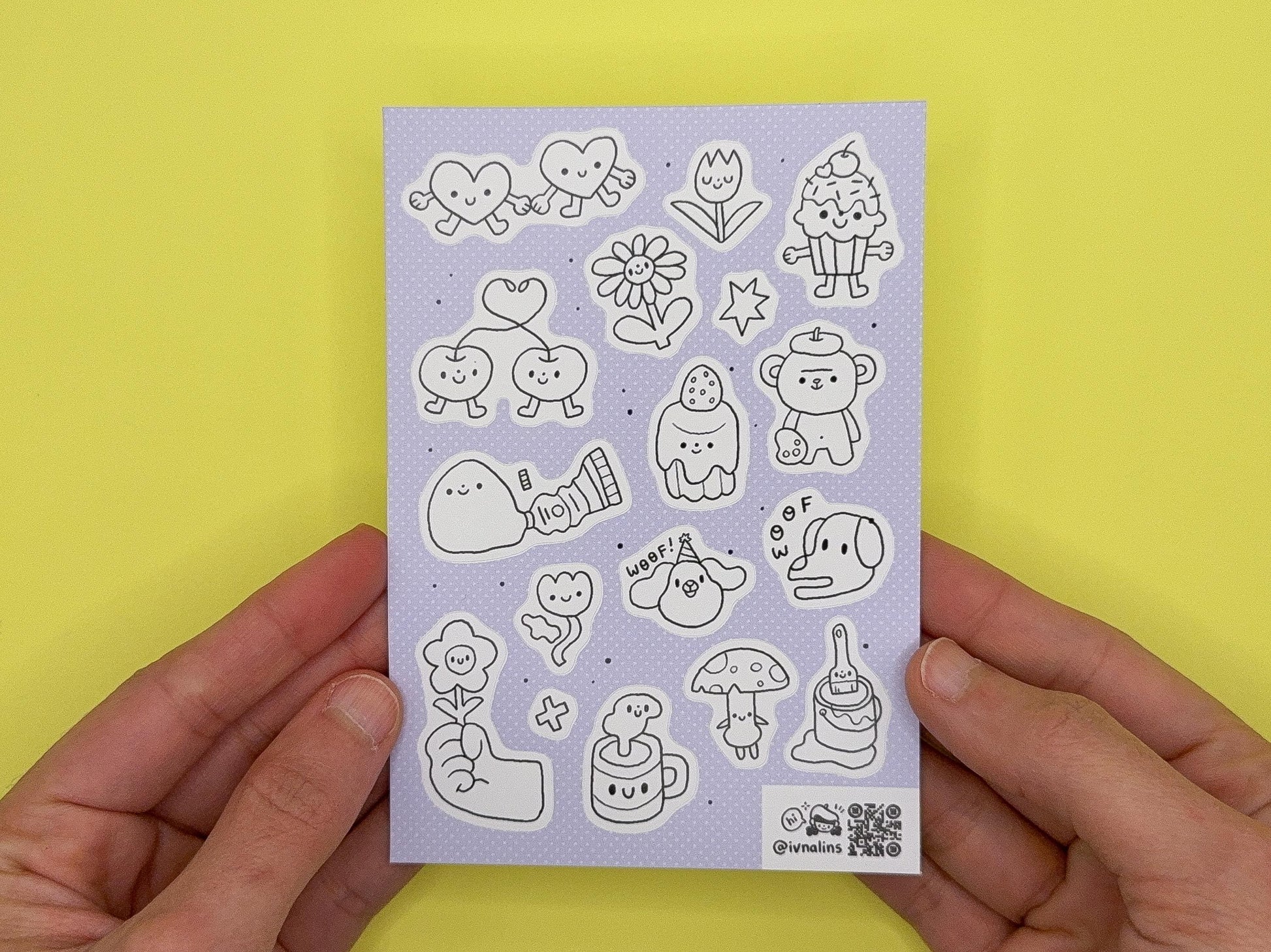 Sheet of cute illustrated stickers held by hands against a yellow background